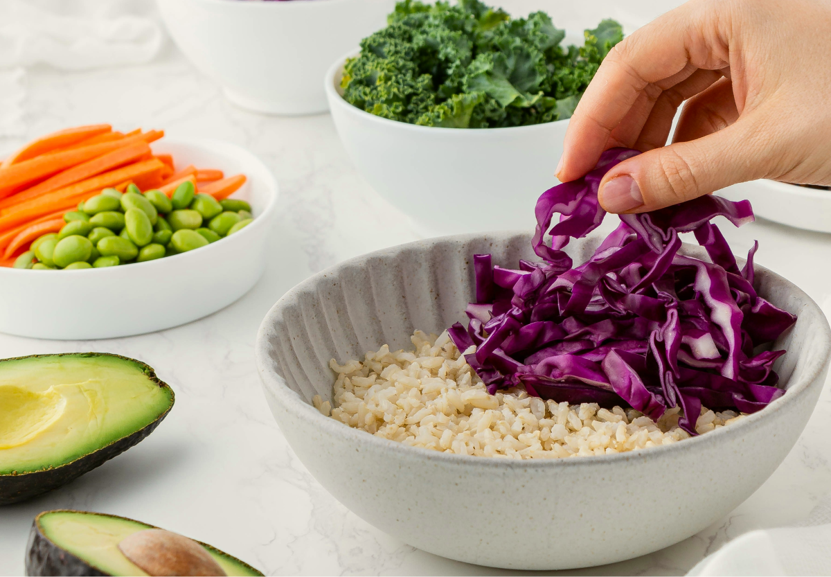 A table with a variety of white bowls filled with colorful vegetables including carrots, purple cabbage, Kale and edamame beans