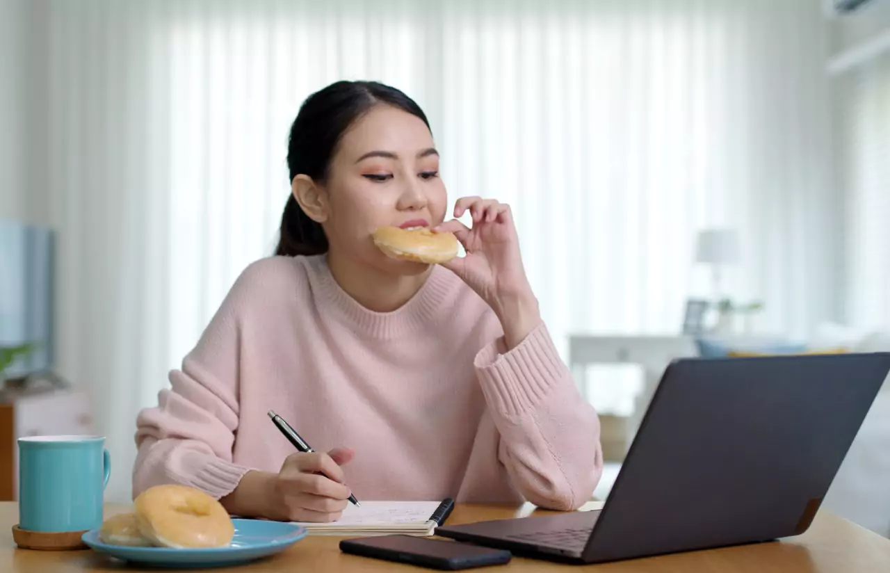 A person working at a laptop eating a donut