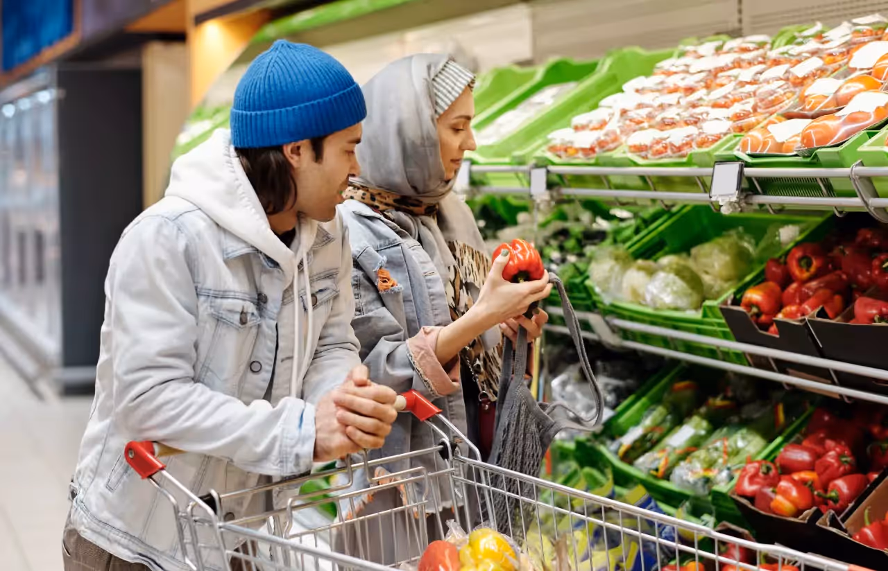 A man and woman at the grocery store, looking at red peppers