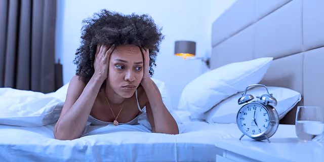 a person laying in bad and looking at a clock 
