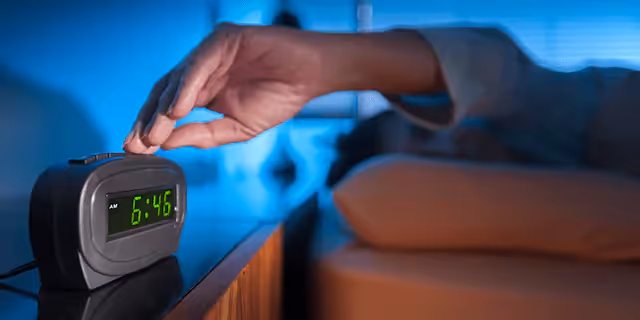 a person laying in bed and turning off an alarm 