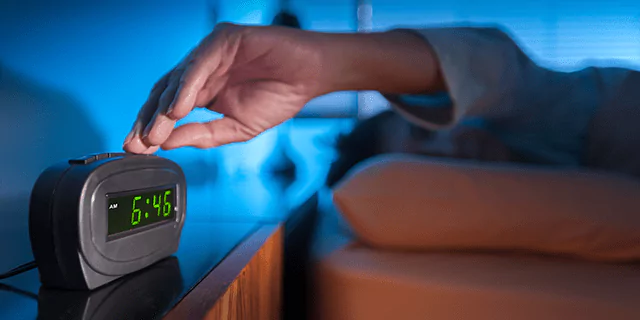 a person laying in bed and turning off an alarm