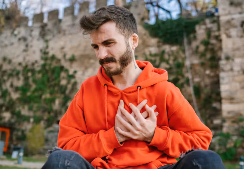 a man sitting down and clutching his chest in pain