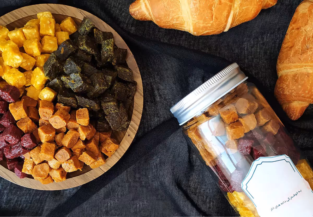 A bowl of dried fruits next to a jar of dried fruits, with croissants in the background