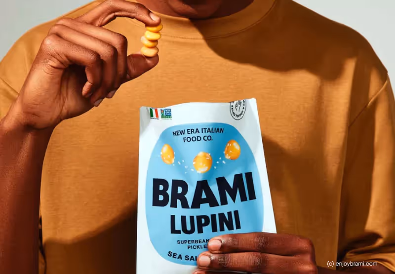 A closeup of someone in an orange t shirt holding a bag of Brami Lupini Beans