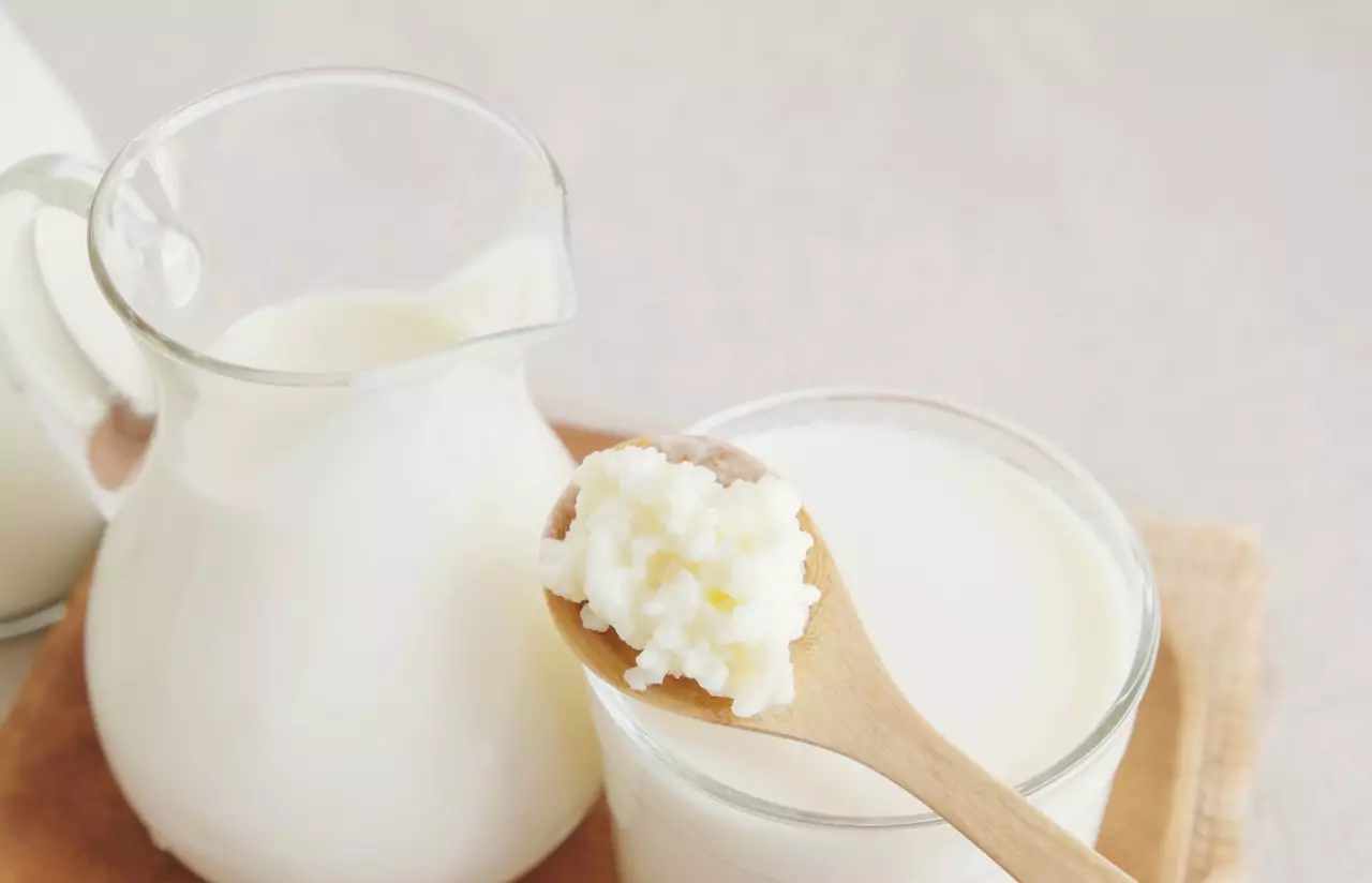 A jar of milk with a measuring cup of milk and a wooden spoon over it with kefirt