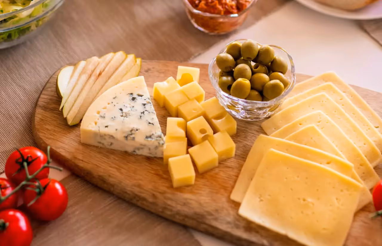 A cheeseboard with types of cheeses and a bowl of olives