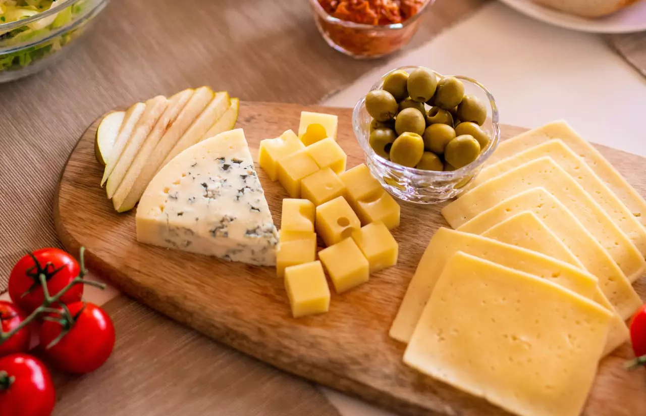 A cheeseboard with types of cheeses and a bowl of olives