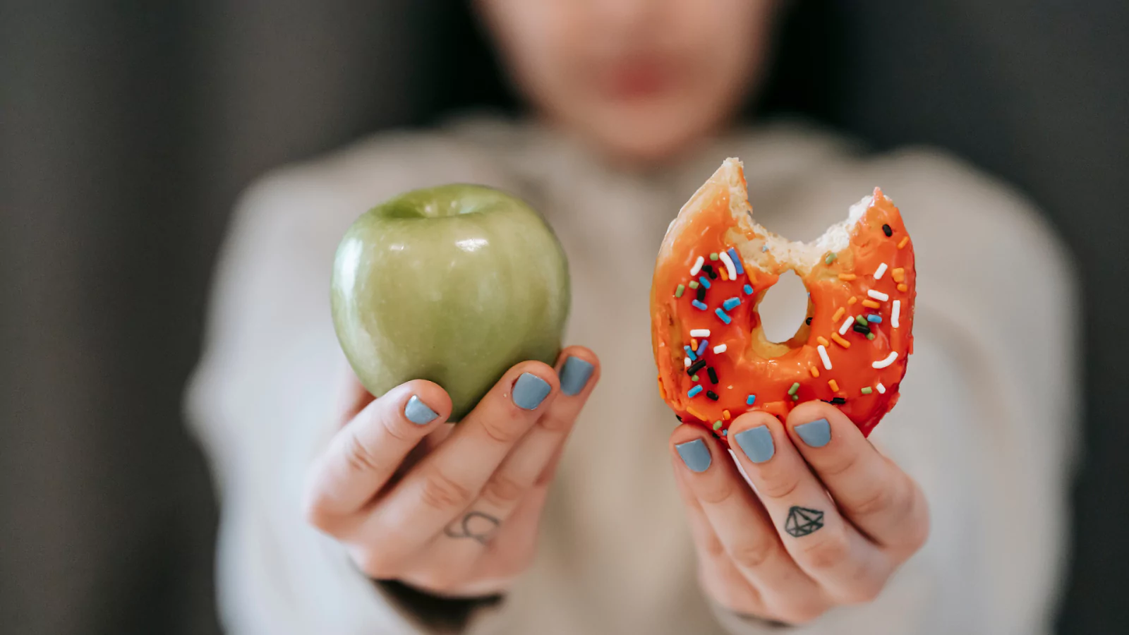 person holding up an apple and donut in their hands