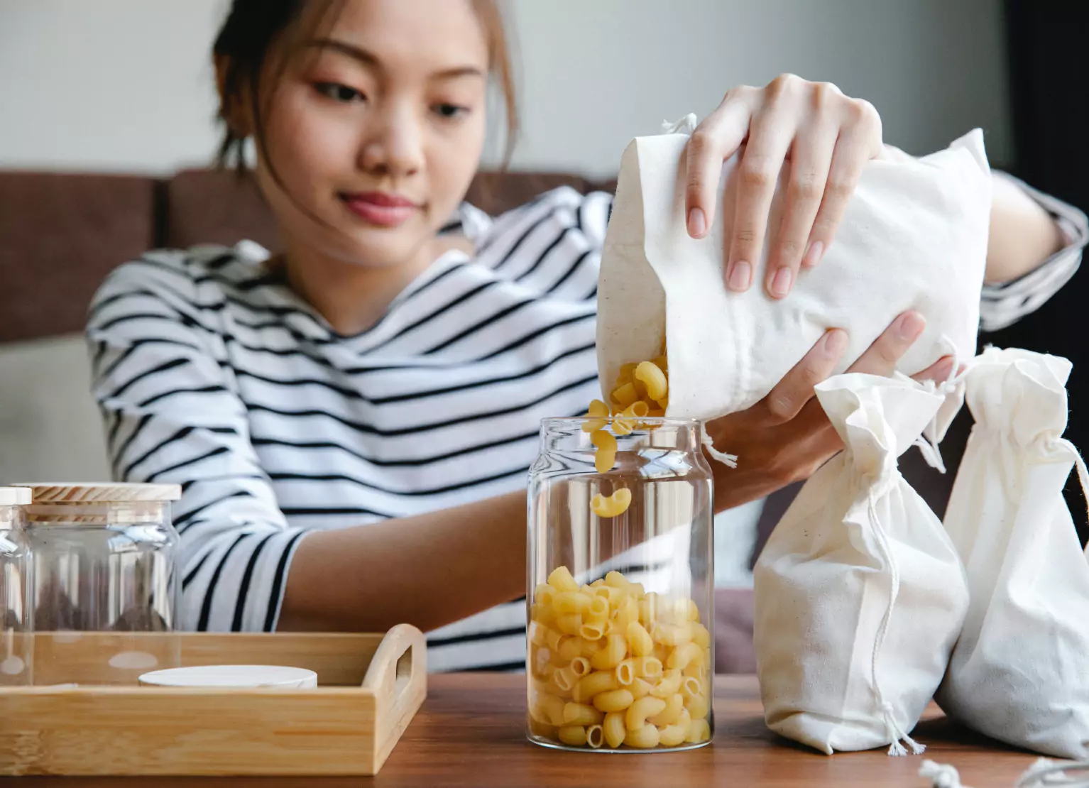 Person pouring dry pasta into glass container