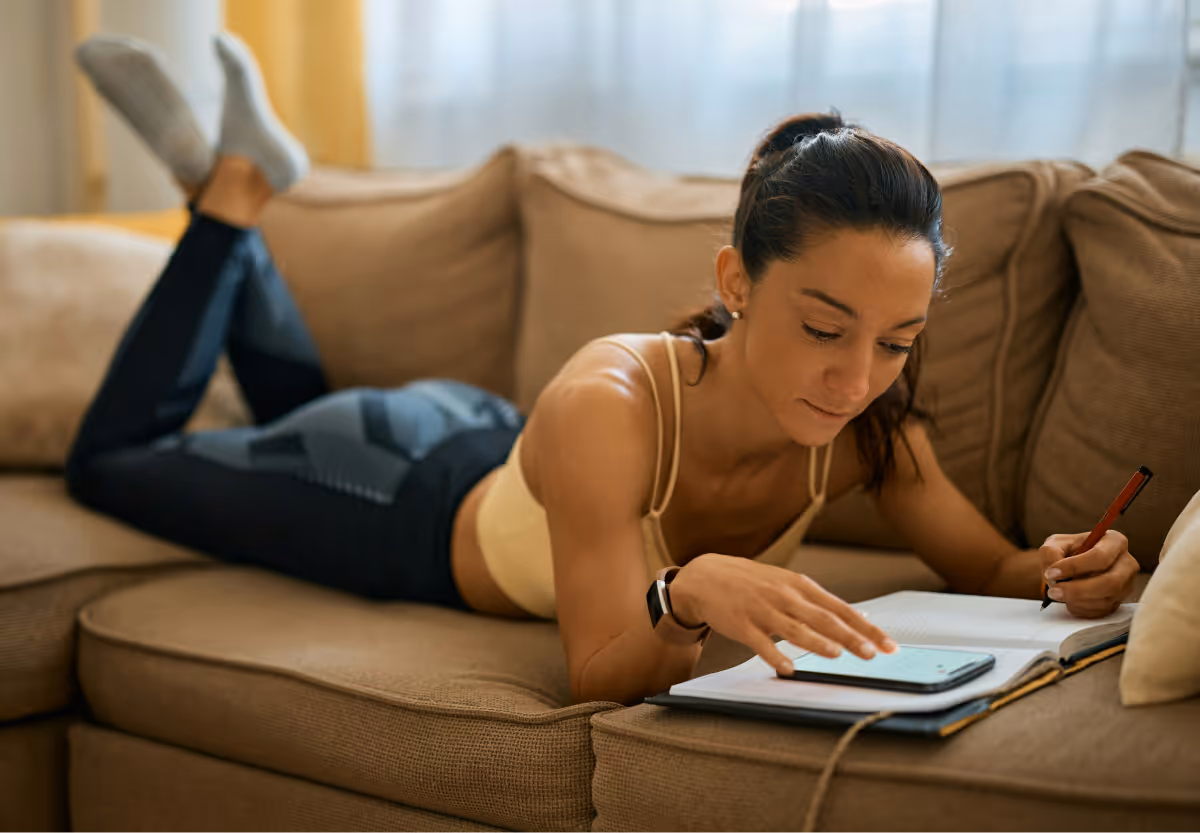 person in workout gear on couch indoors writing in journal