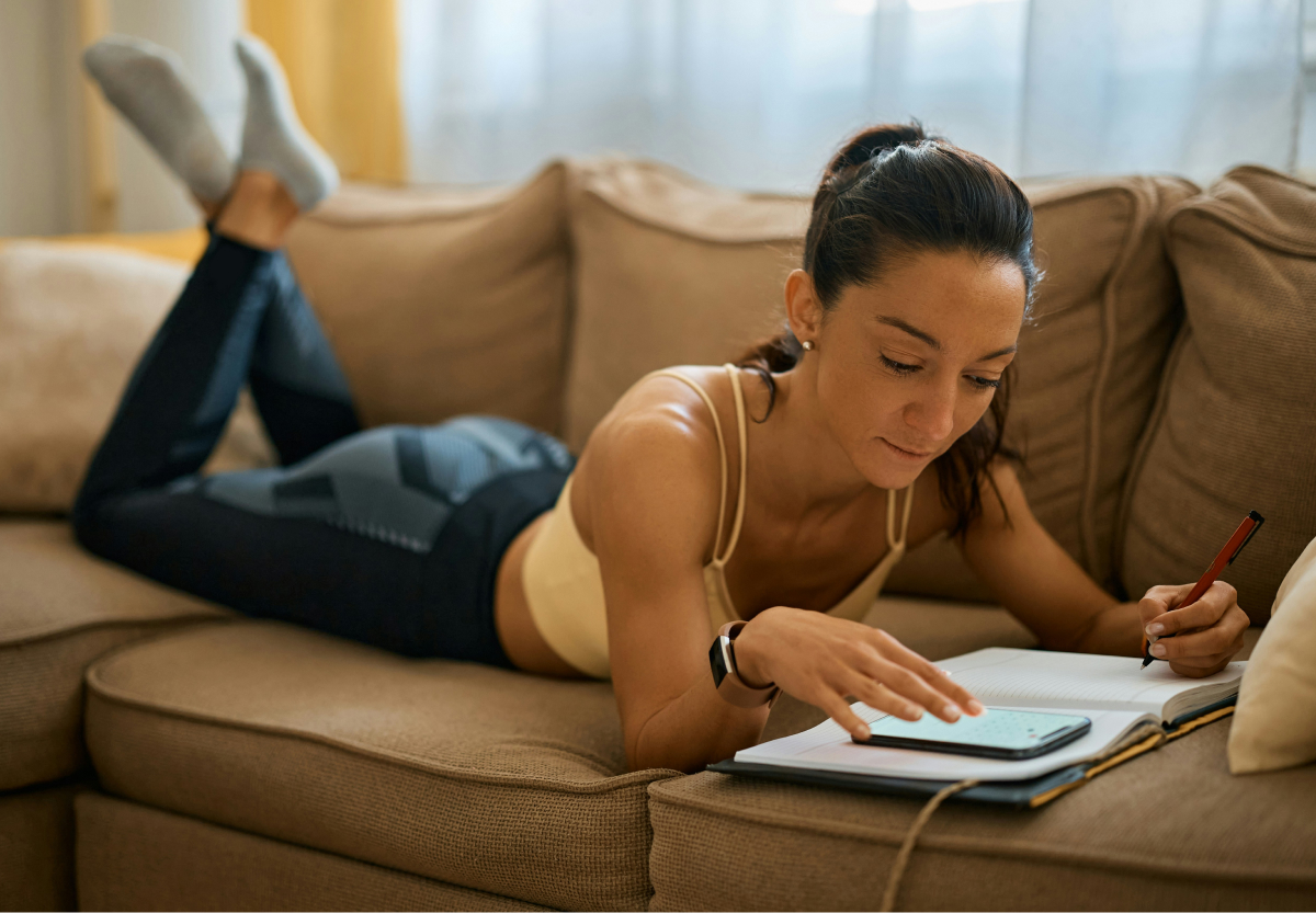 person in workout gear on couch indoors writing in journal