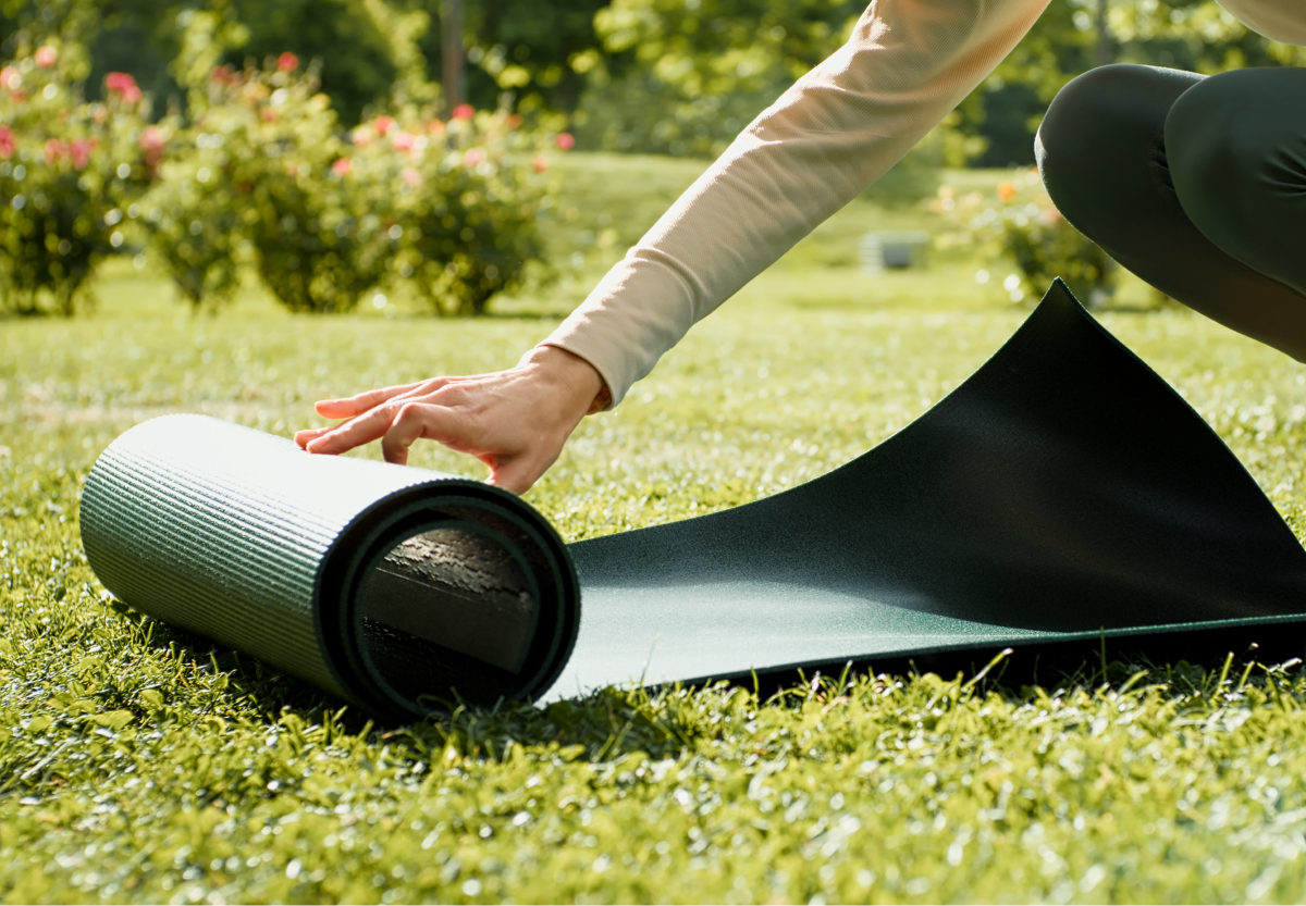 someone's hand in long-sleeves rolling out a green exercise mat on the grass outdoors