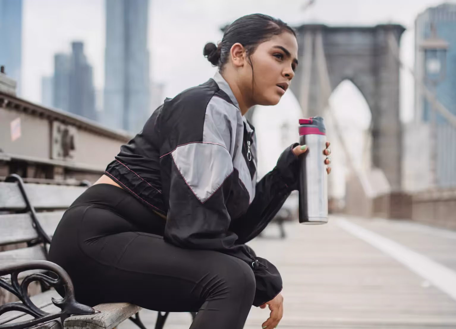 a person sitting on bench with workout gear drinking from water bottle