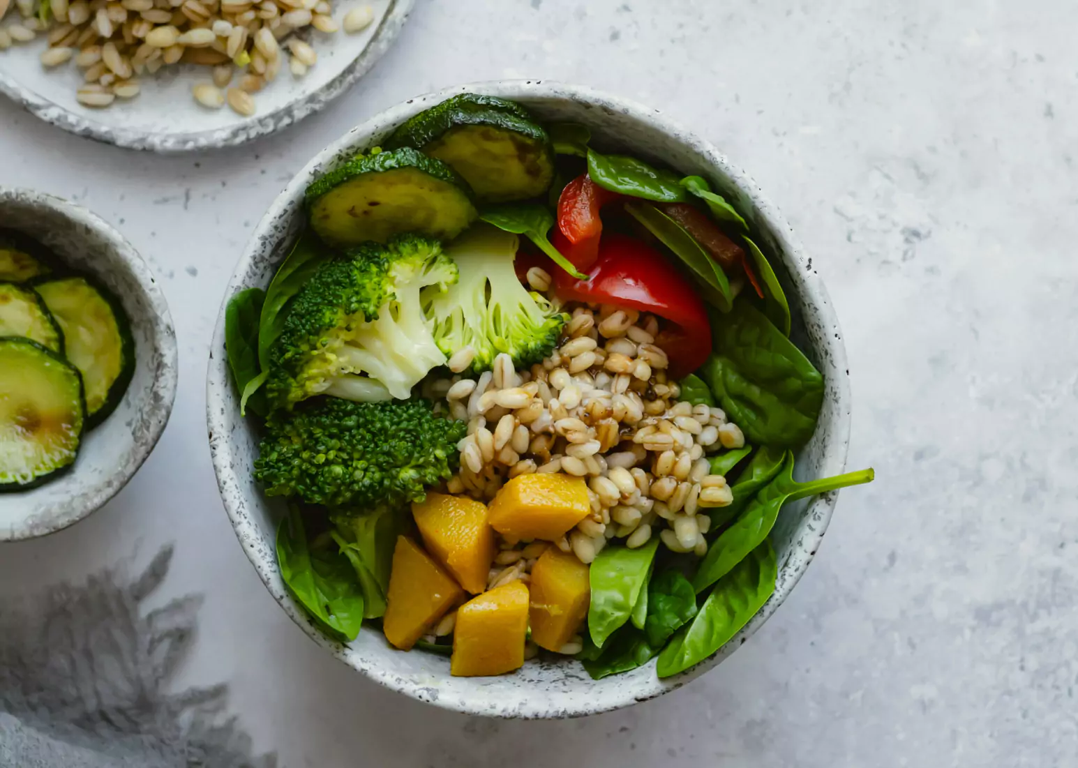 A bowl of fresh vegetables and grains on a grey backdrop