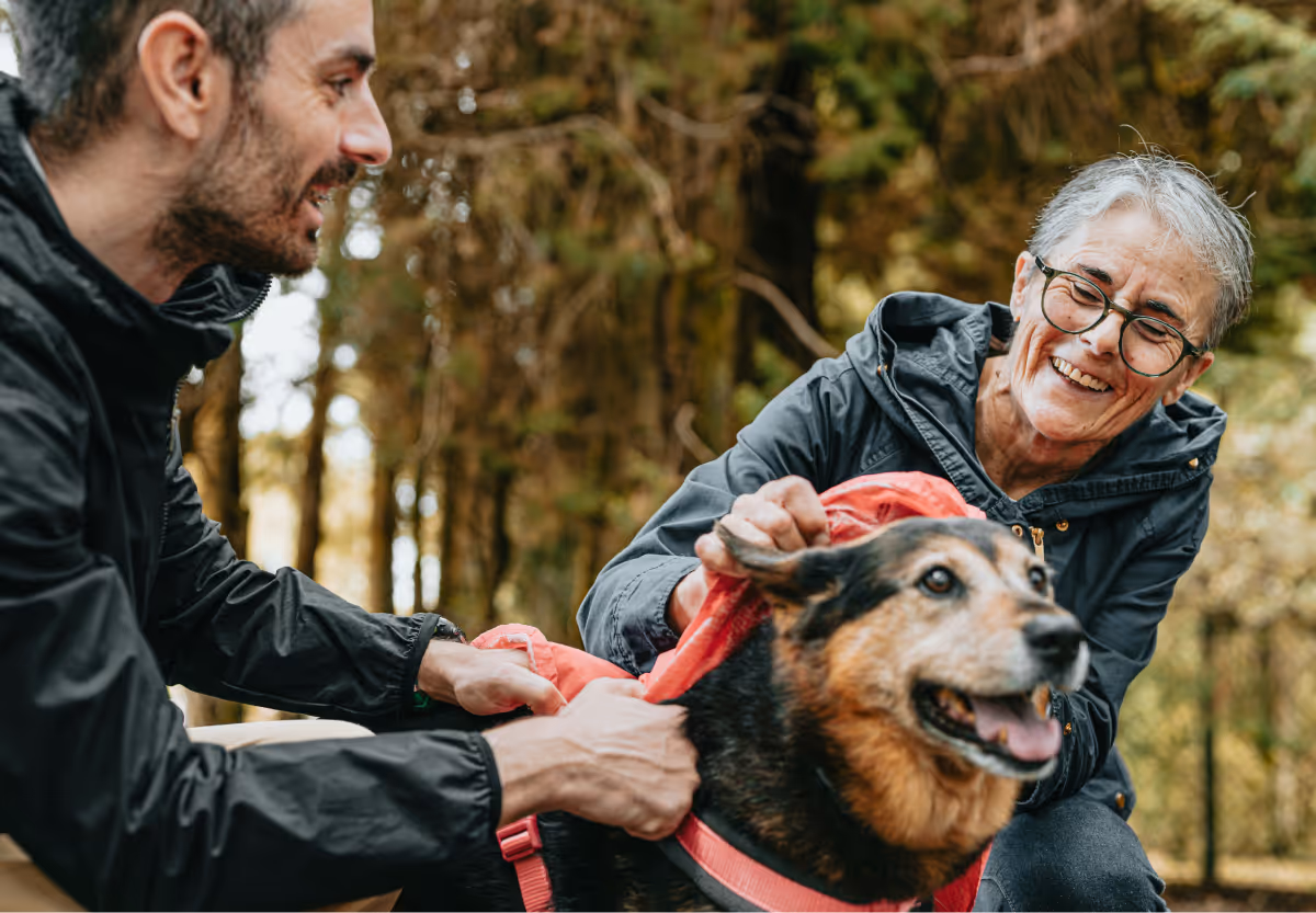 Two people outdoors, with a dog in a red leash