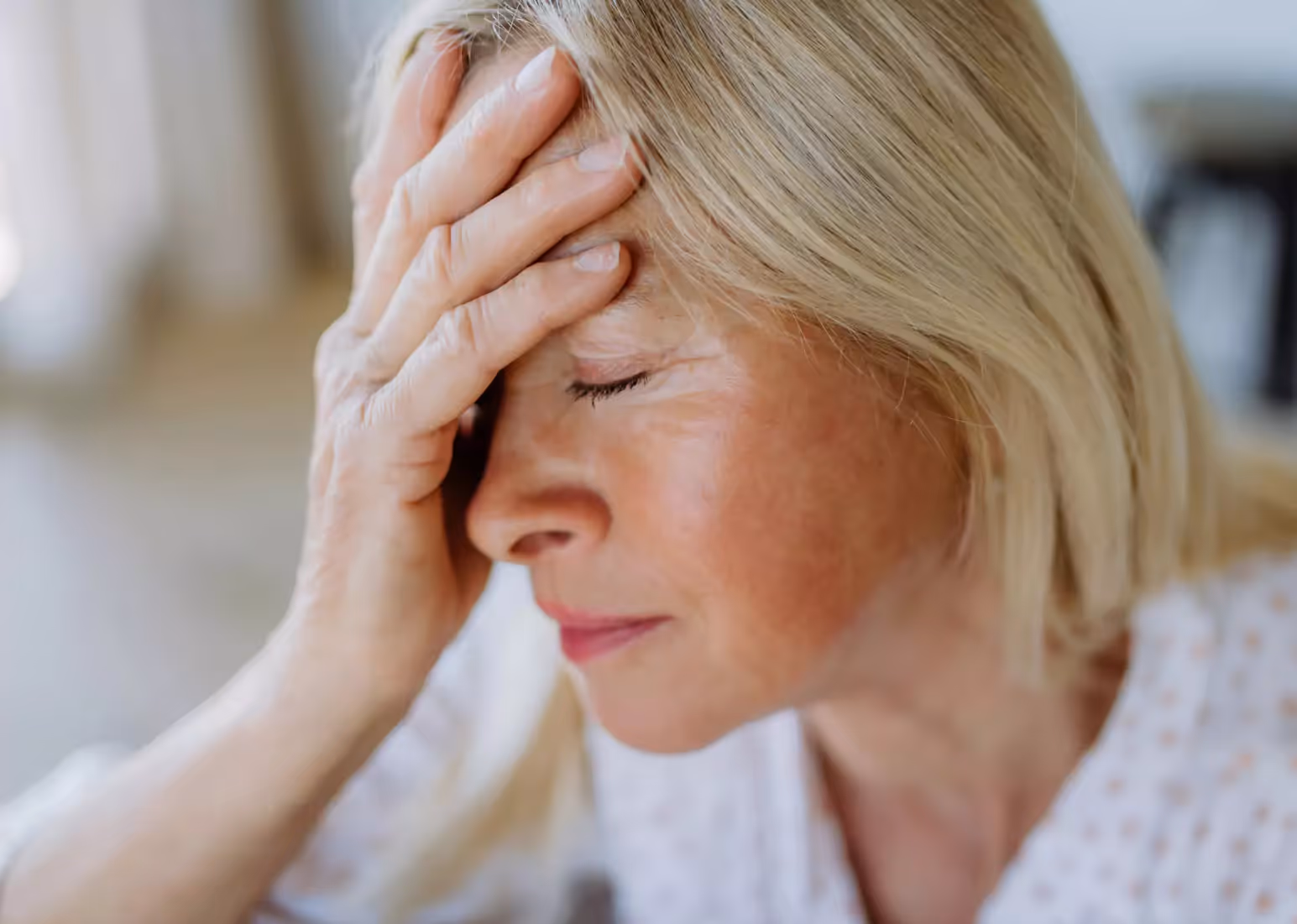 A closeup of someone in a white shirt, holding their head in their hand
