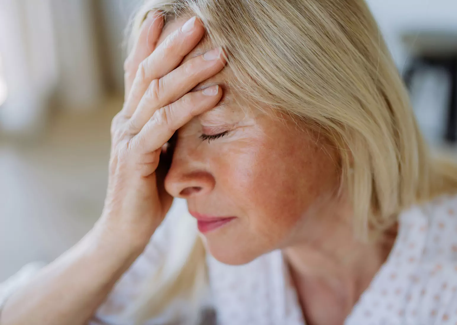 A closeup of someone in a white shirt, holding their head in their hand