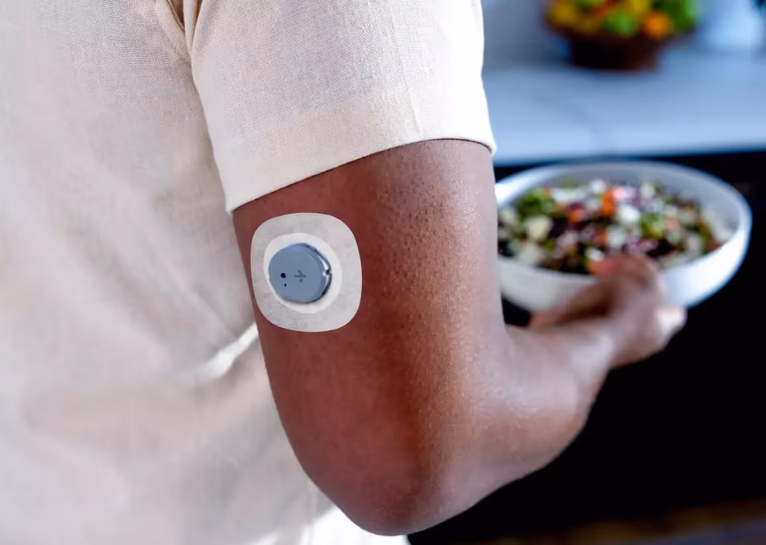 A closeup of the arm of a person wearing a cgm sensor, activating it with a mobile phone 