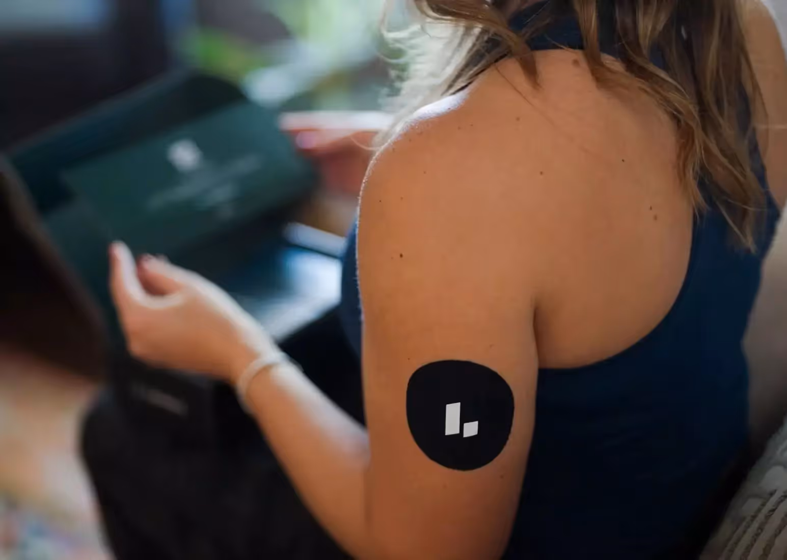 A close-up of someone with a CGM on their arm, holding a phone looking at their glucose levels
