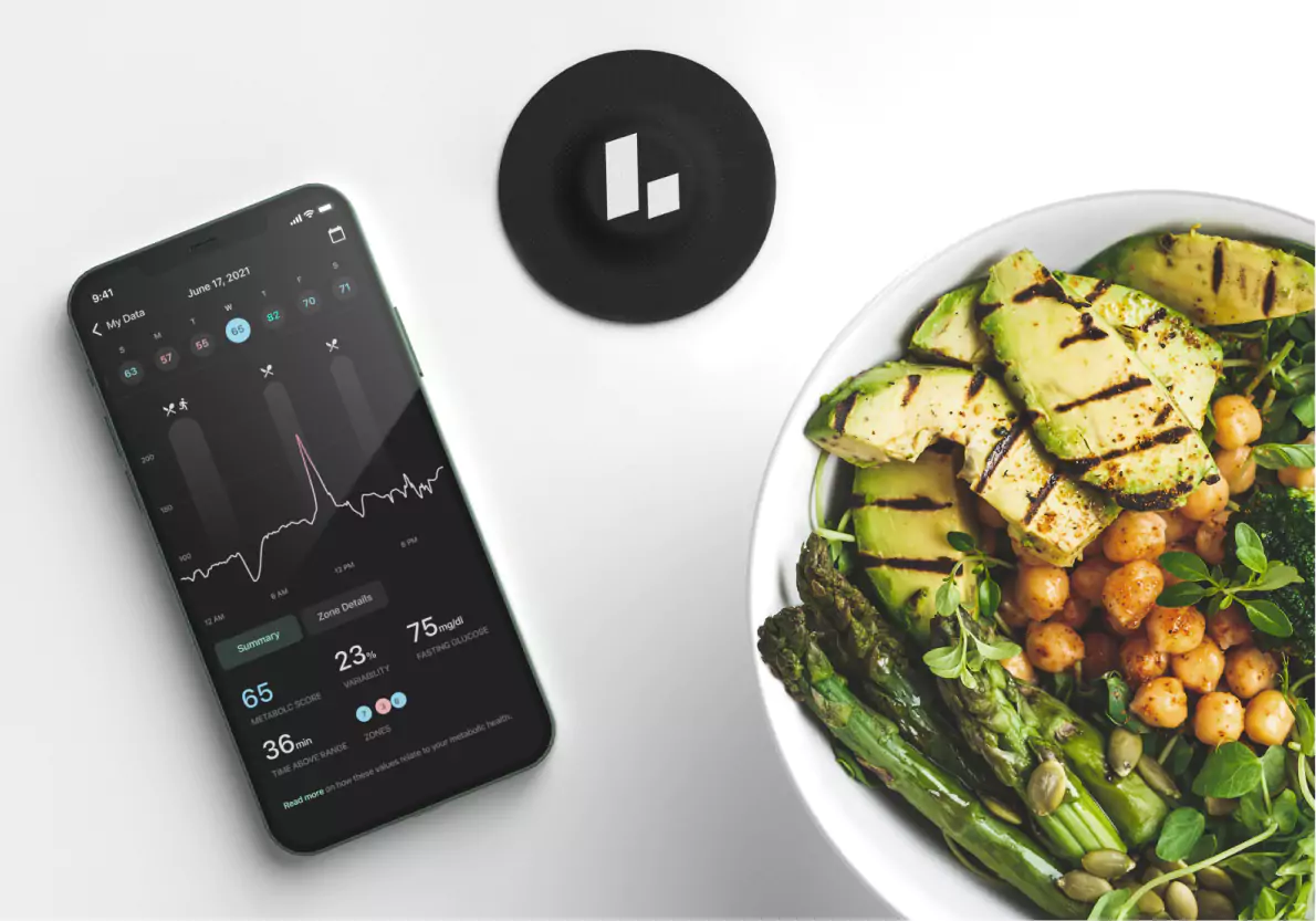 Dining table with Levels Health app on phone and veggie bowl with avocado and broccoli