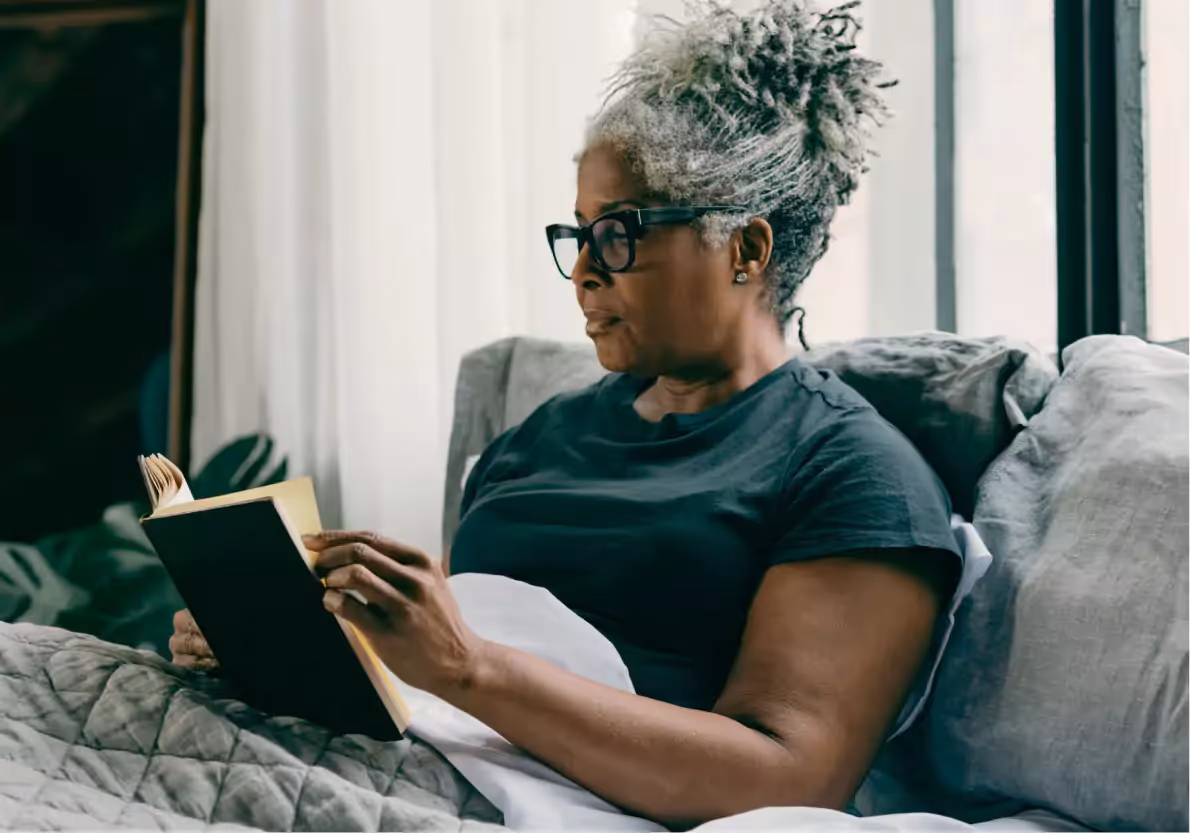 A person  in bed reading a book, wearing a CGM or glucose biosensor