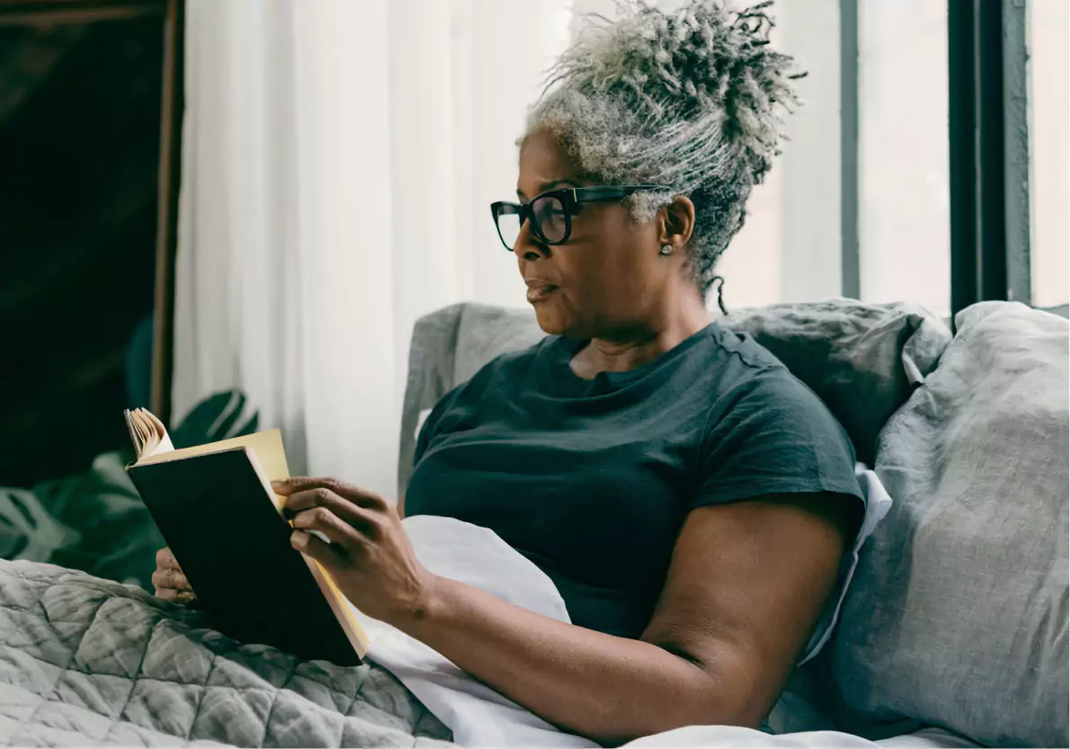 A person in bed reading a book, wearing a CGM or glucose biosensor