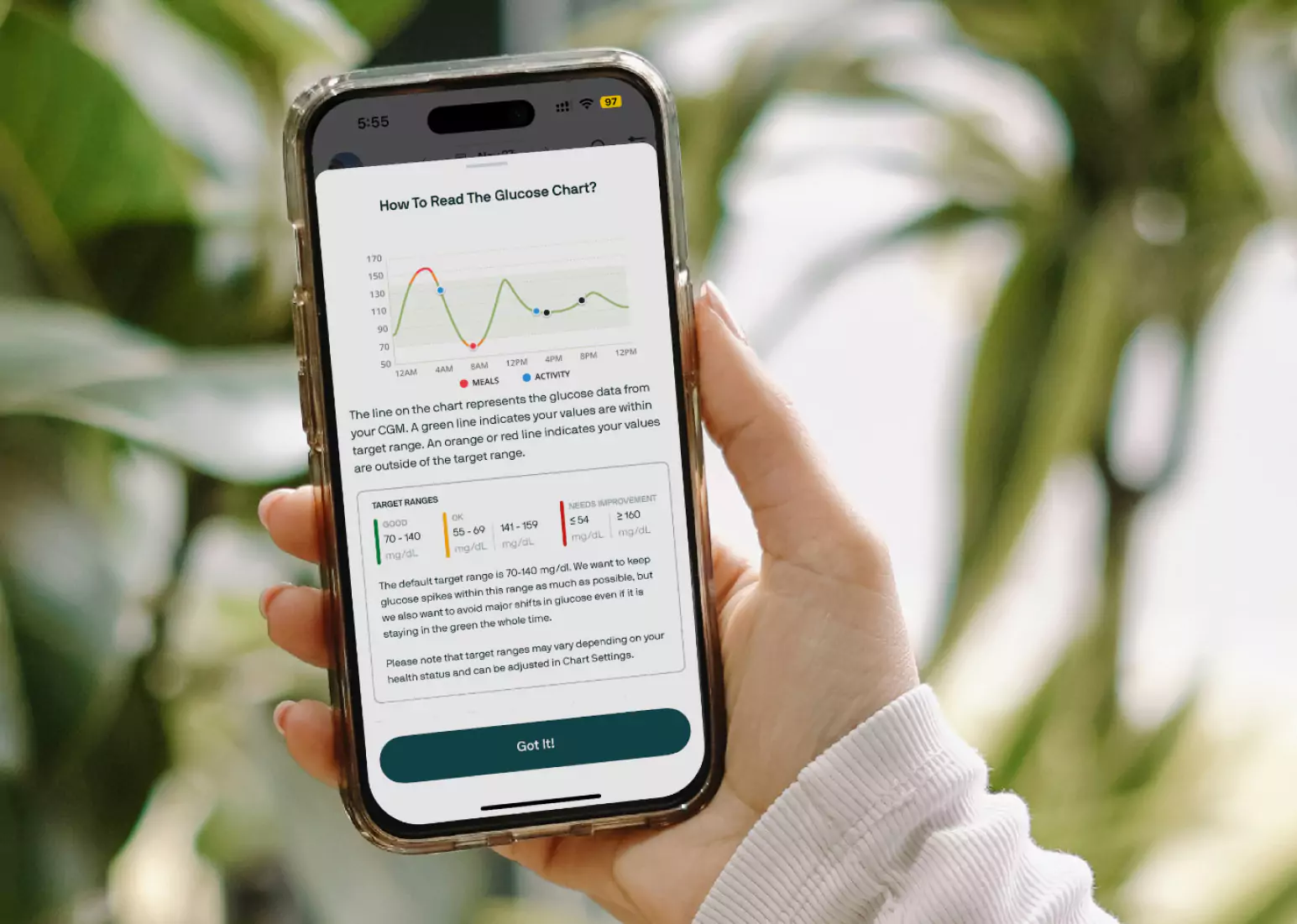 A hand holding a phone with the Nutrisense app open, reading a blood sugar log