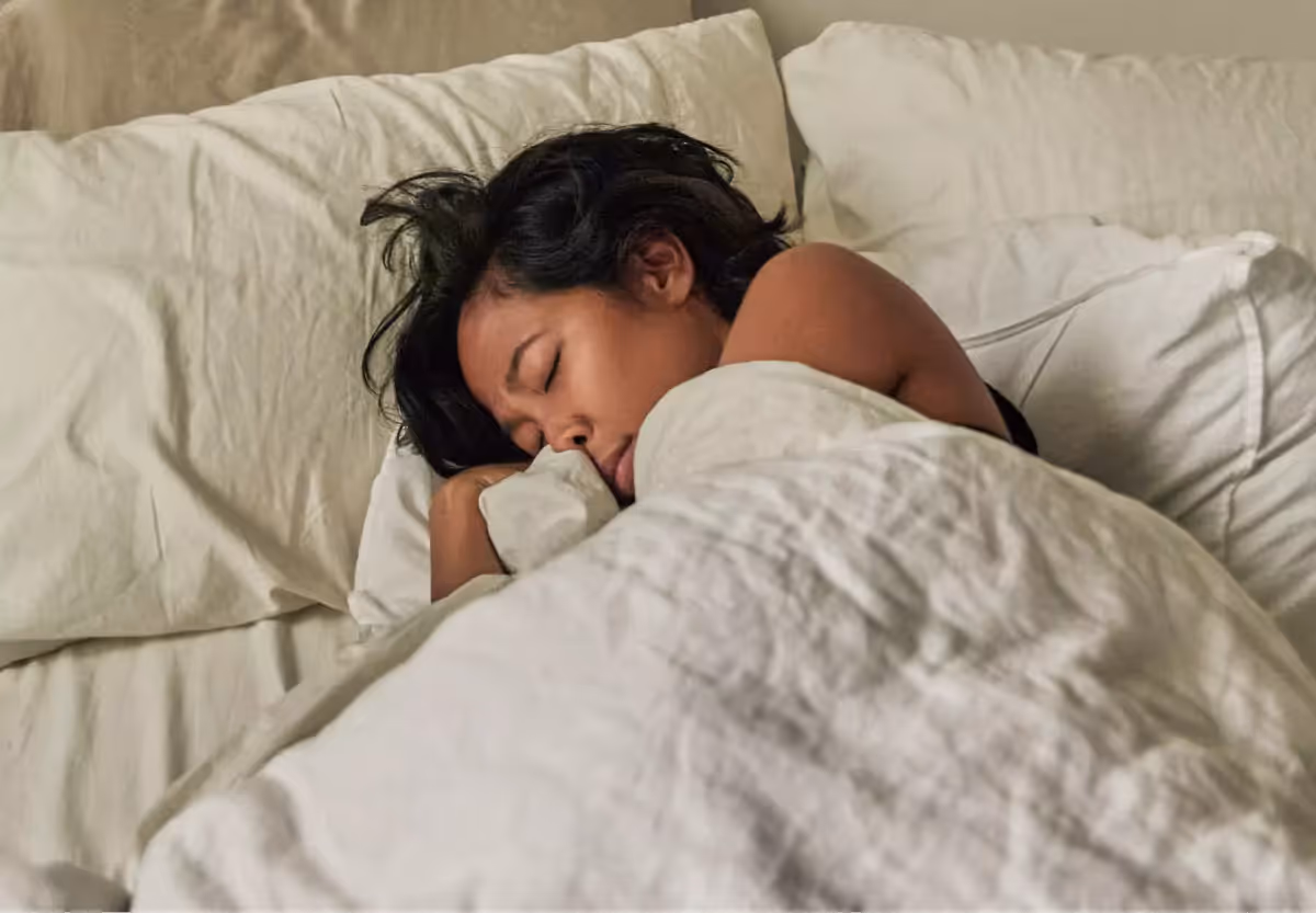 A person curled up under cream colored blankets in bed