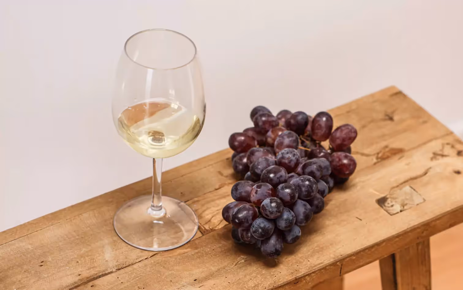 A glass of white wine and a bunch of grapes on a wooden platform