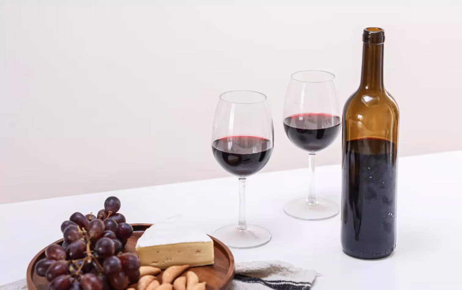 Two glasses and a bottle of red wine alongside grapes