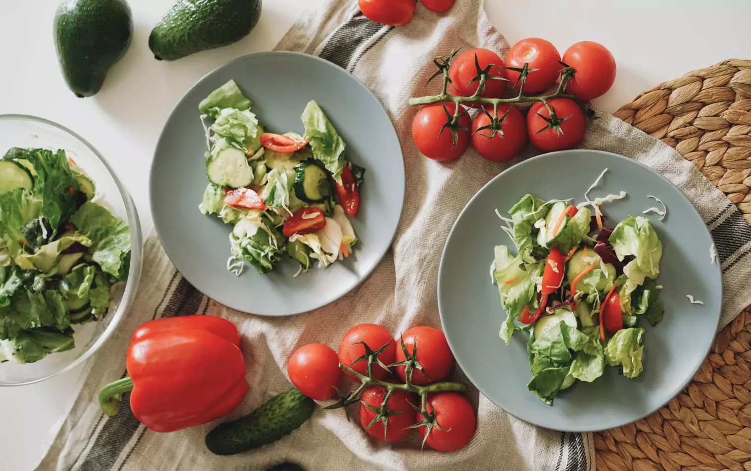 Plates of salad surrounded by tomatoes and avocados