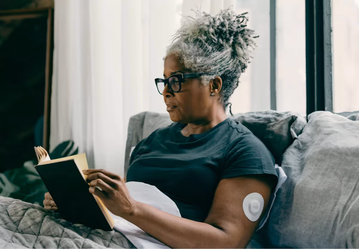 A woman wearing the Nutrisense CGM patch reading a book