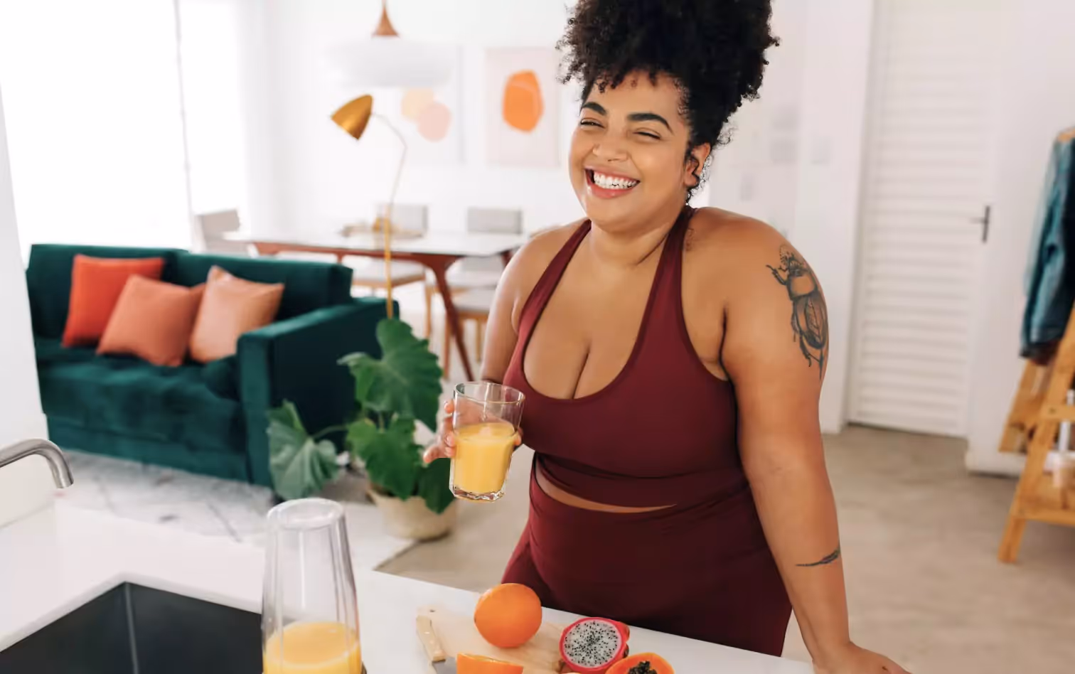 A woman in athletic wear holding a glass of orange juice and laughing