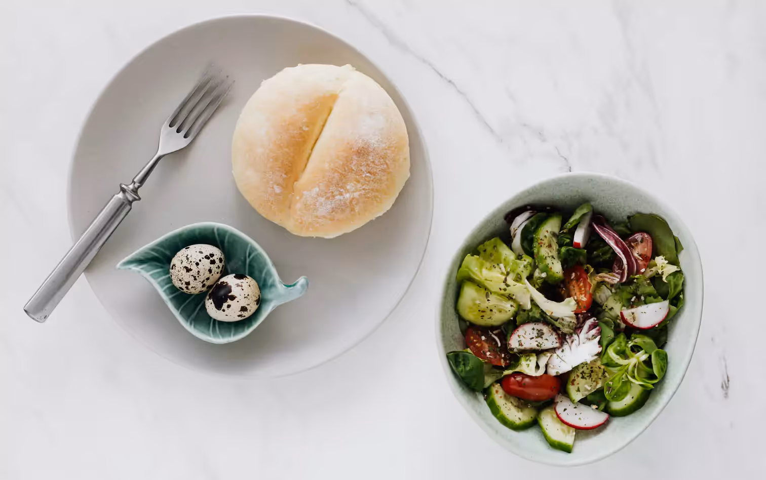 eggs and a bun on a plate and a bowl of salad