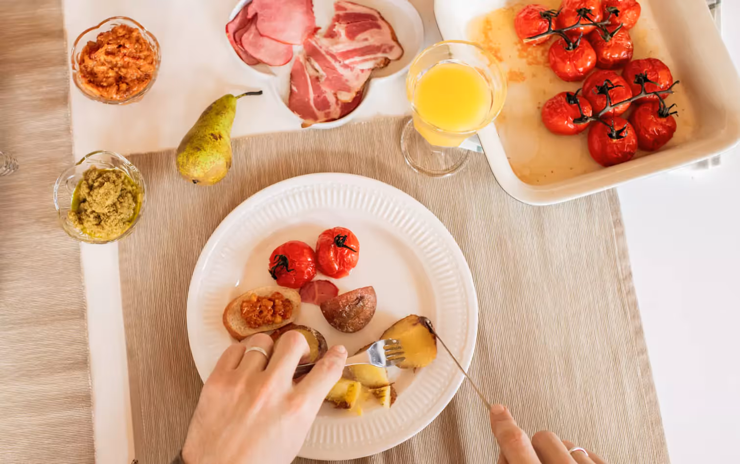 a person eating baked potatoes, tomatoes and drinking orange juice  