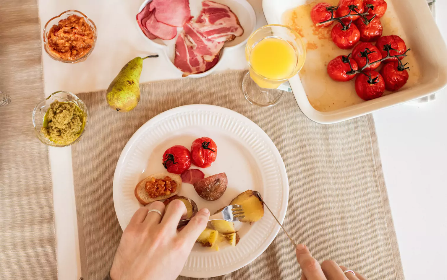 a person eating baked potatoes, tomatoes and drinking orange juice