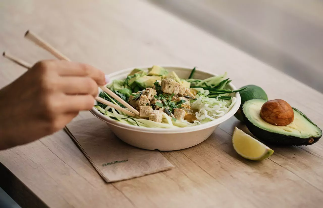 a bowl of tofu and veggies and an avocado on a table