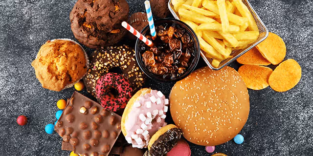 fries, a burger, muffins, a bar of chocolate, donuts and a glass of soda