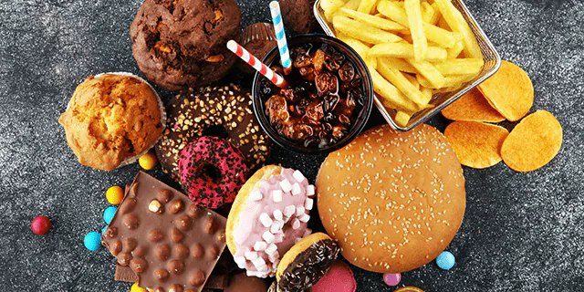 fries, a burger, muffins, a bar of chocolate, donuts and a glass of soda