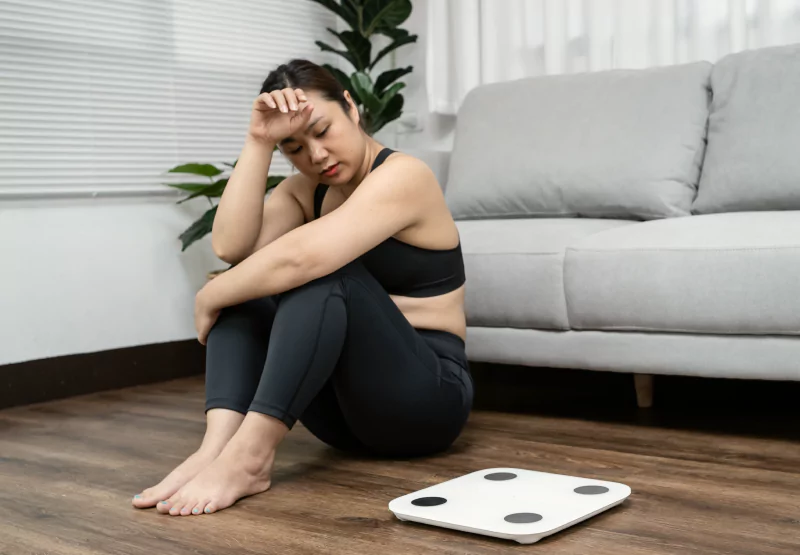 a girl in workout clothes sitting next to a scale