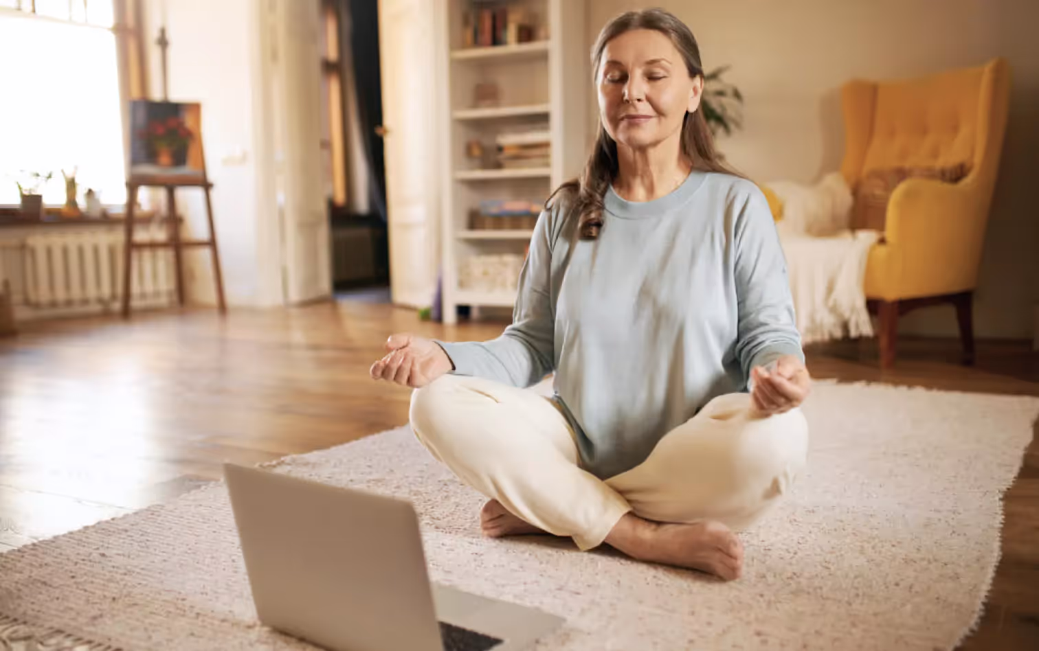 a person sitting on the floor and meditating in front of a laptop 