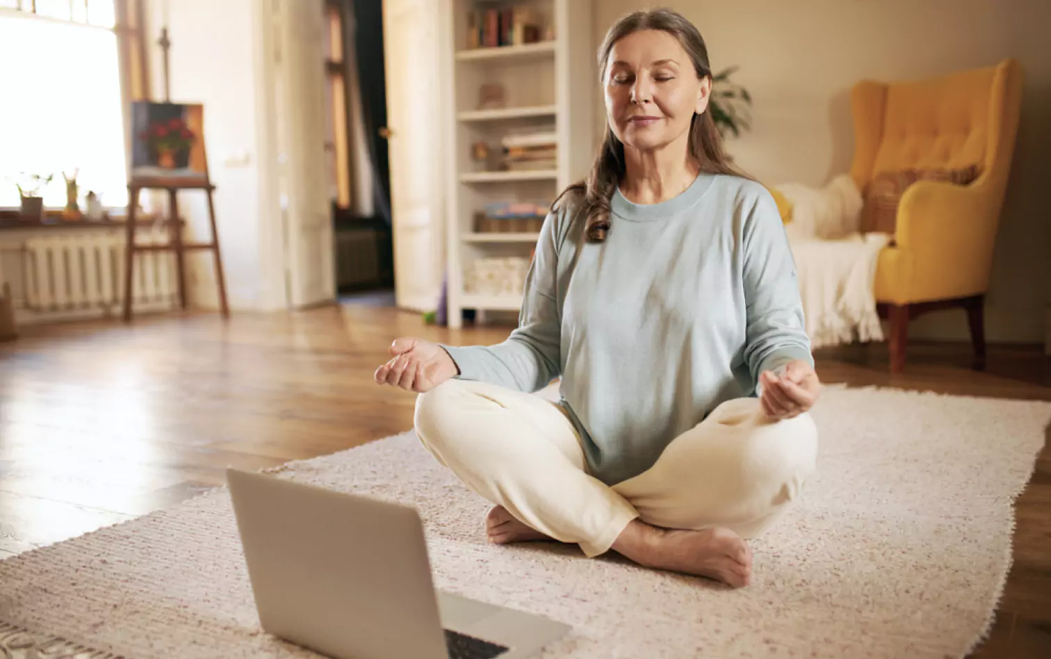 a person sitting on the floor and meditating in front of a laptop