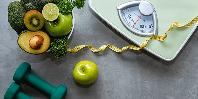 a scale, a tape measure, dumbbells and a bowl of veggies and fruits