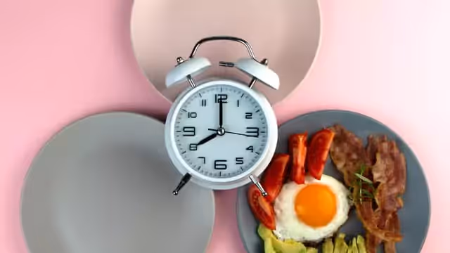 two empty plate and a plate of bacon, a fried egg, avocado and tomatoes and a clock