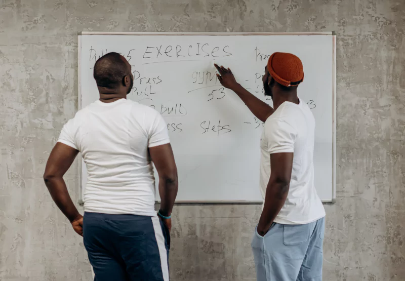 two men looking at a workout plan on a white board