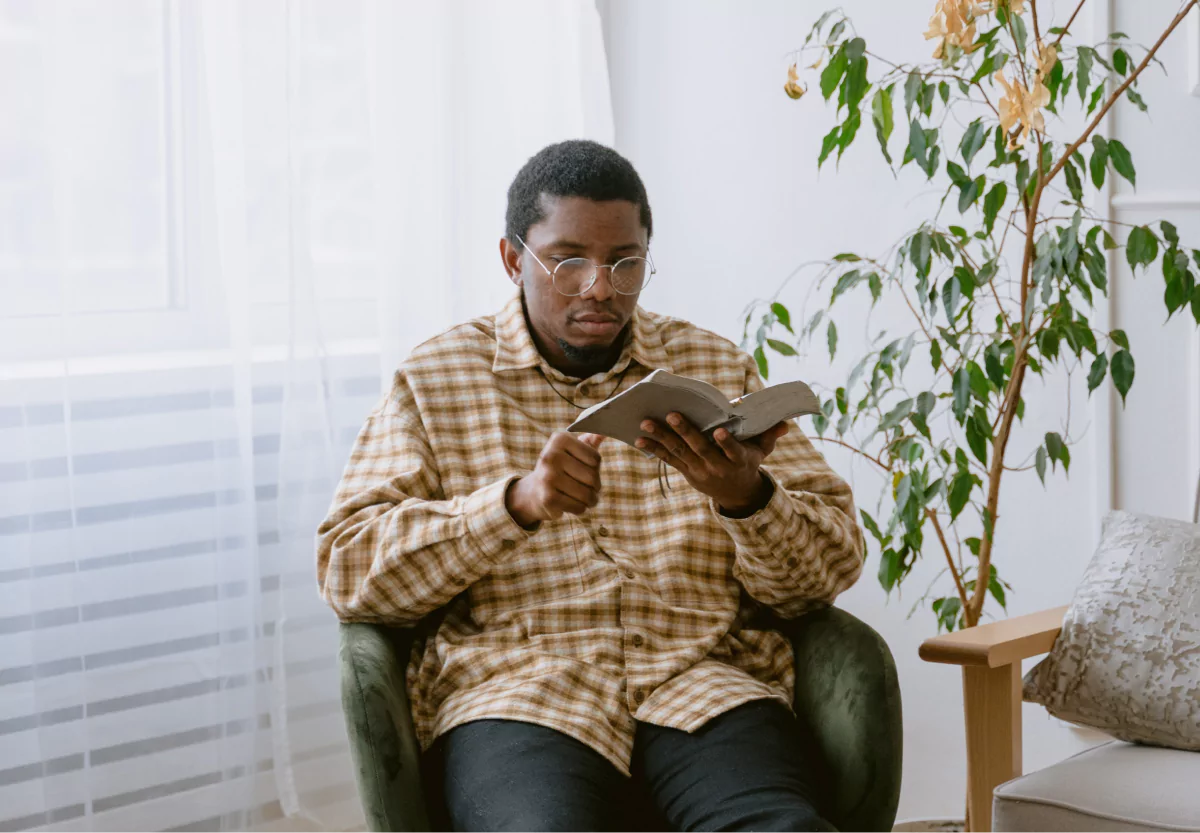 a body reading a book next to a plant