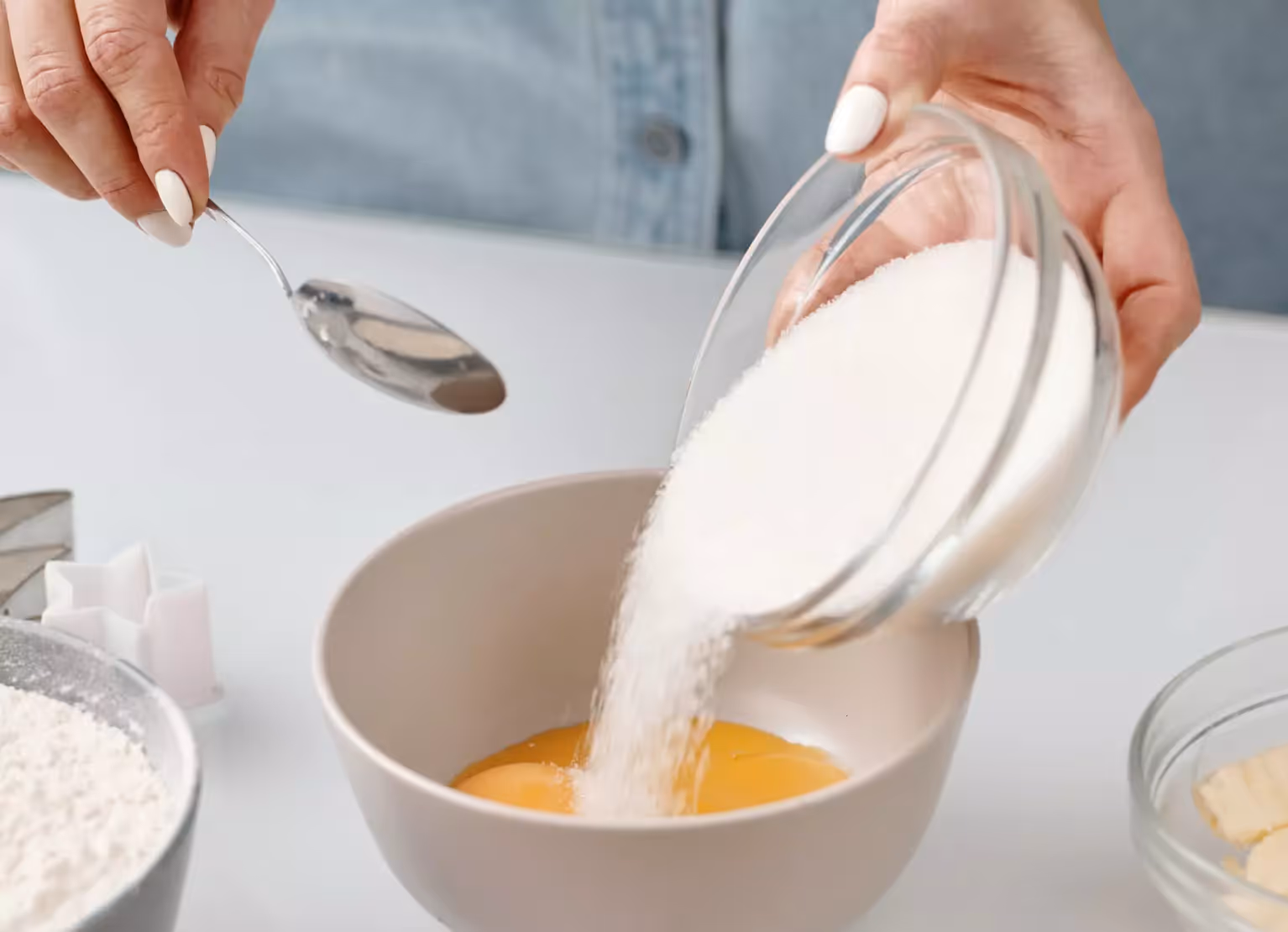 Person adding sugar to eggs in a bowl