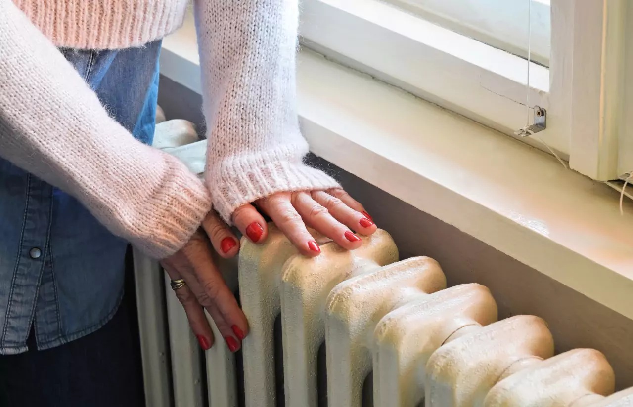 person's hands on a radiator near a window