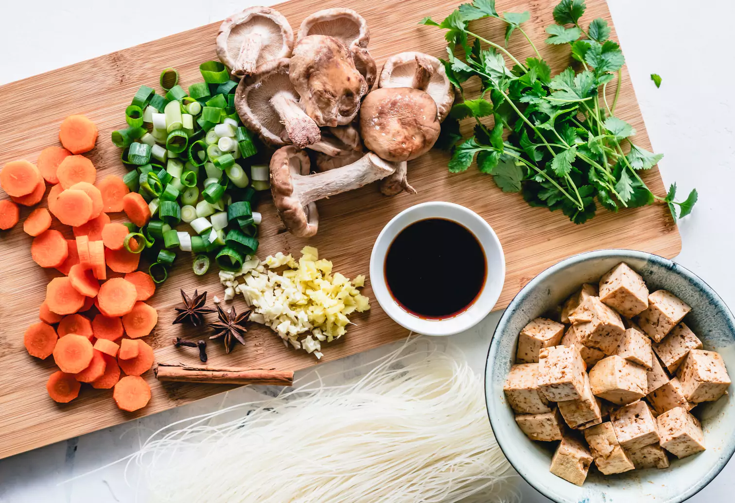 carrots, leek, mushrooms, parsley, tofu and noodles on a cutting board